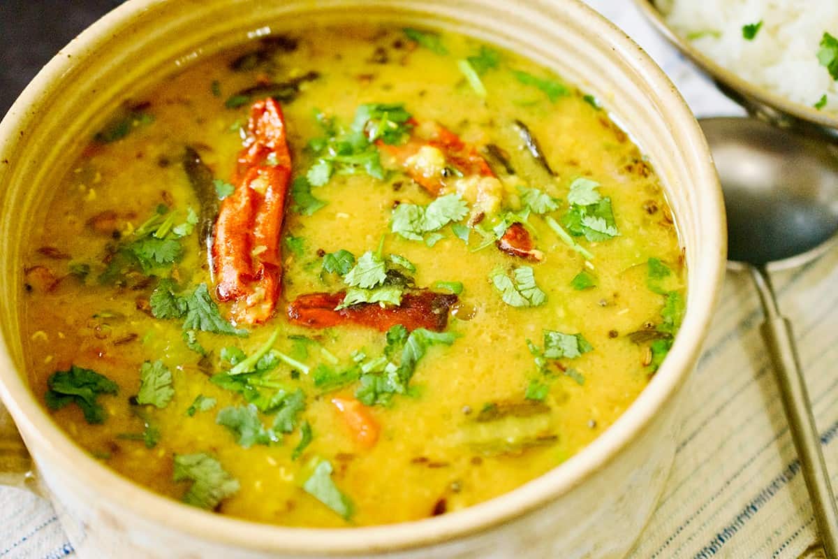 A neutral colored pottery bowl is filled with tempered Lentil Curry (Khatti dal). 