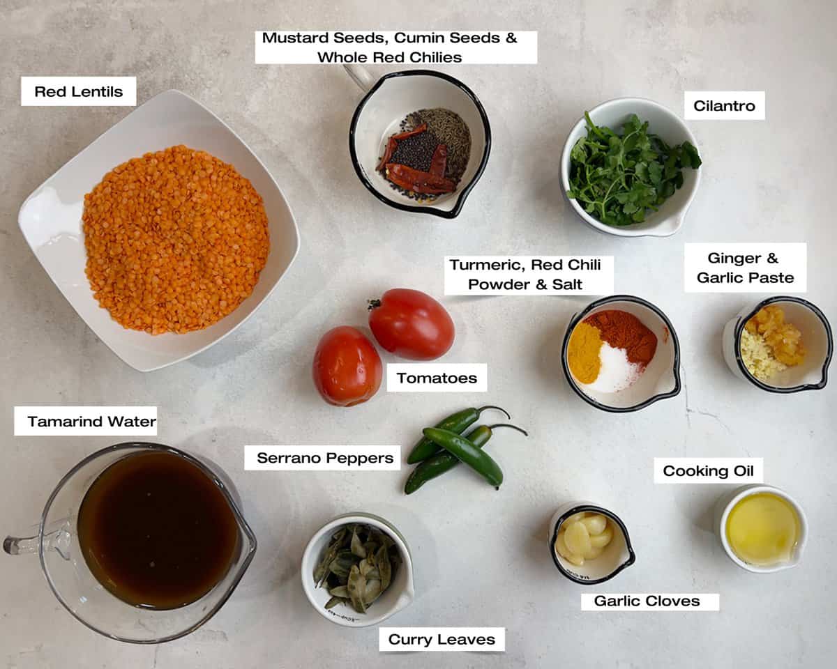 A white kitchen counter is layered with bowls filled with the ingredients to cook a lentil curry (khatti dal) in assorted sizes.