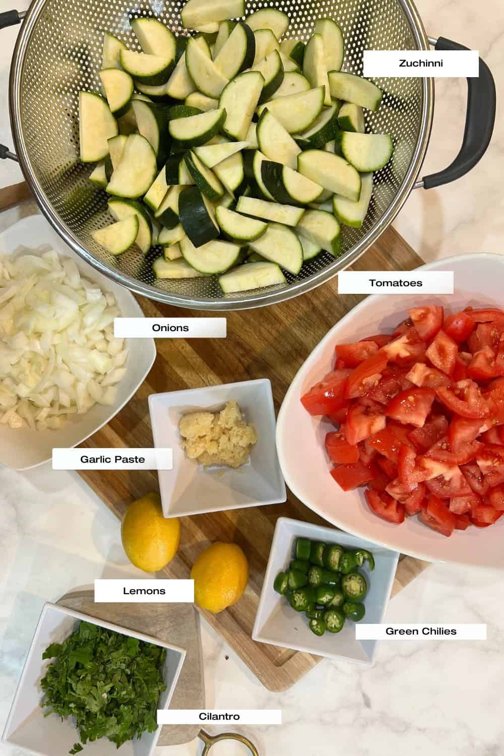 white board with bowls of zucchini, onions, tomatoes, garlic paste, lemons, green chilies and cilantro.