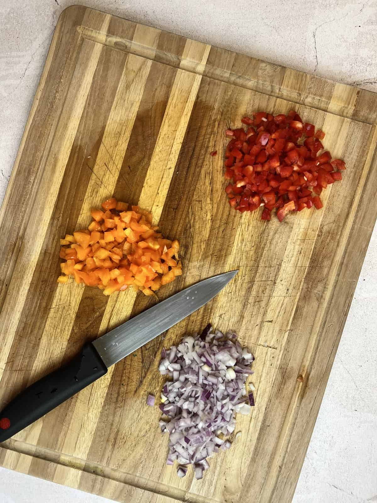 chopping board with red and yellow peppers and purple onion chopped.
