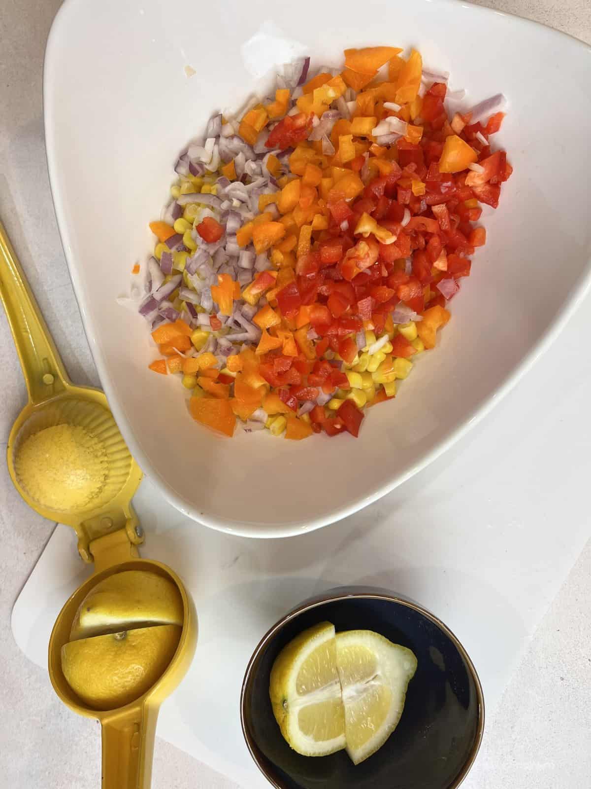 white bowl with corn,peppers and onion and a lemon in a squeezer.