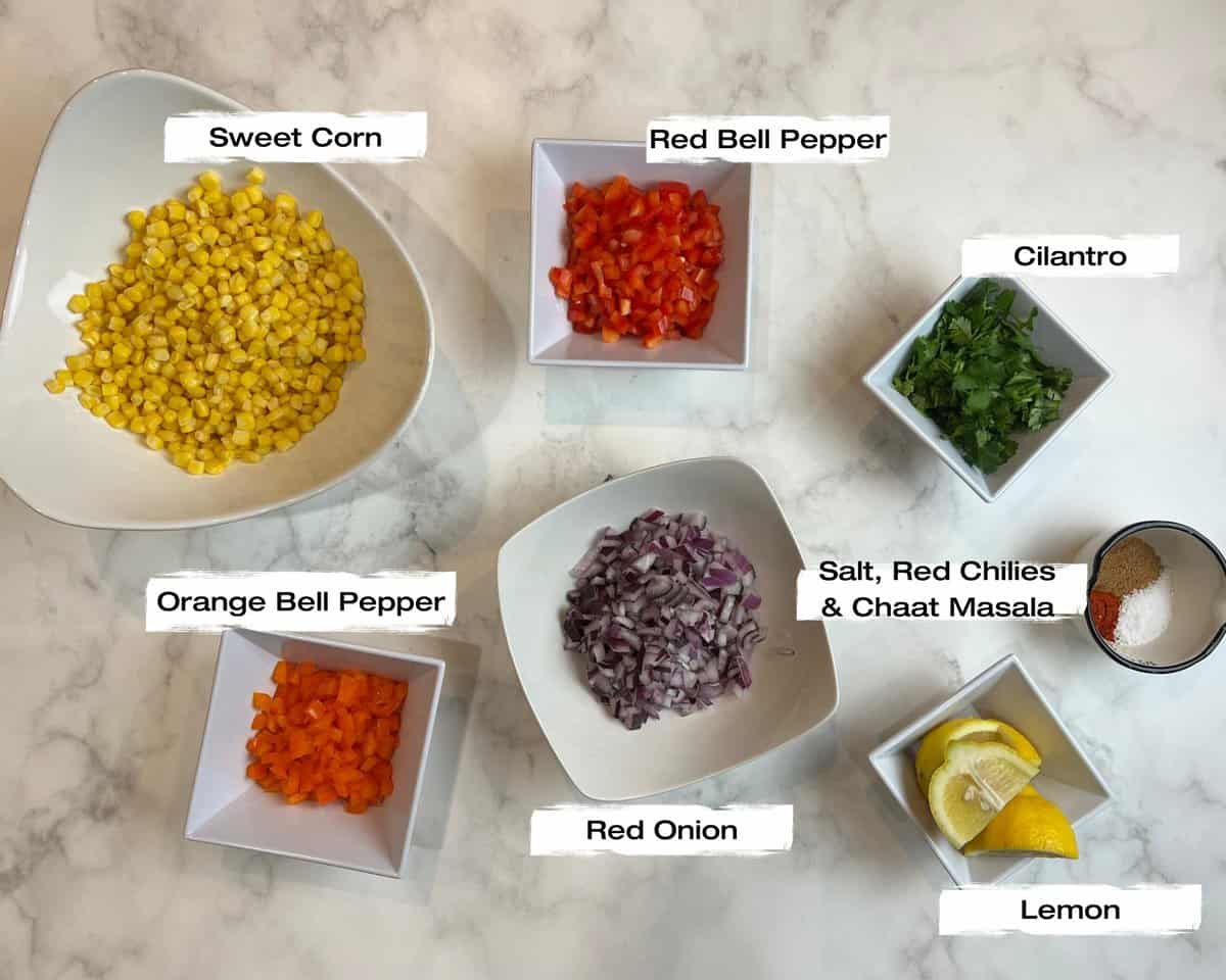 white marble surface with bowls filled with corn, red onion, orange and red bell pepper and lemons.