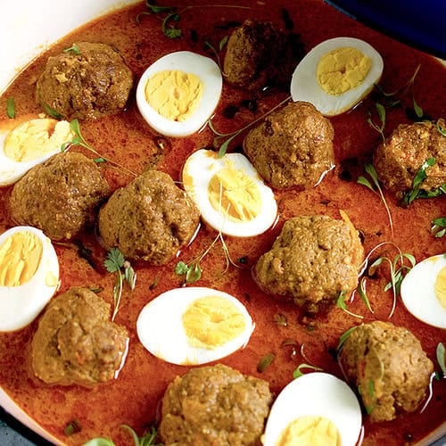 A cooked kofta curry garnished with cilantro microgreens is in a blue and white skillet.