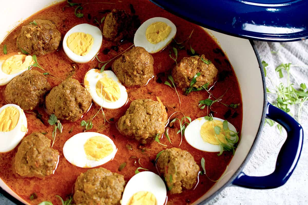 A freshly cooked Kofta curry with boiled eggs, garnished with cilantro microgreens is in a blue and white skillet.