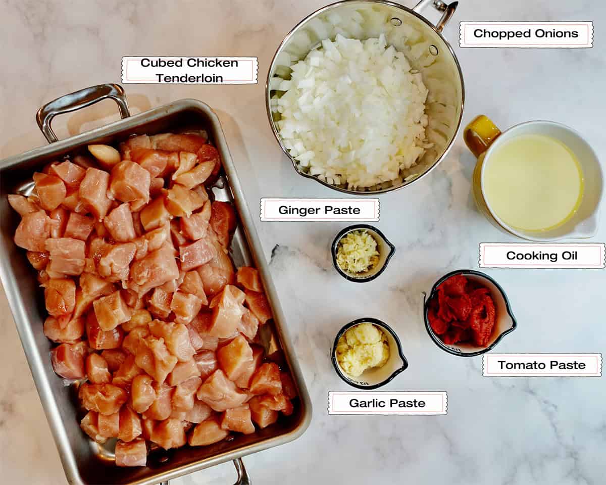 Ingredients to cook chicken makhani are placed on a white chicken counter.