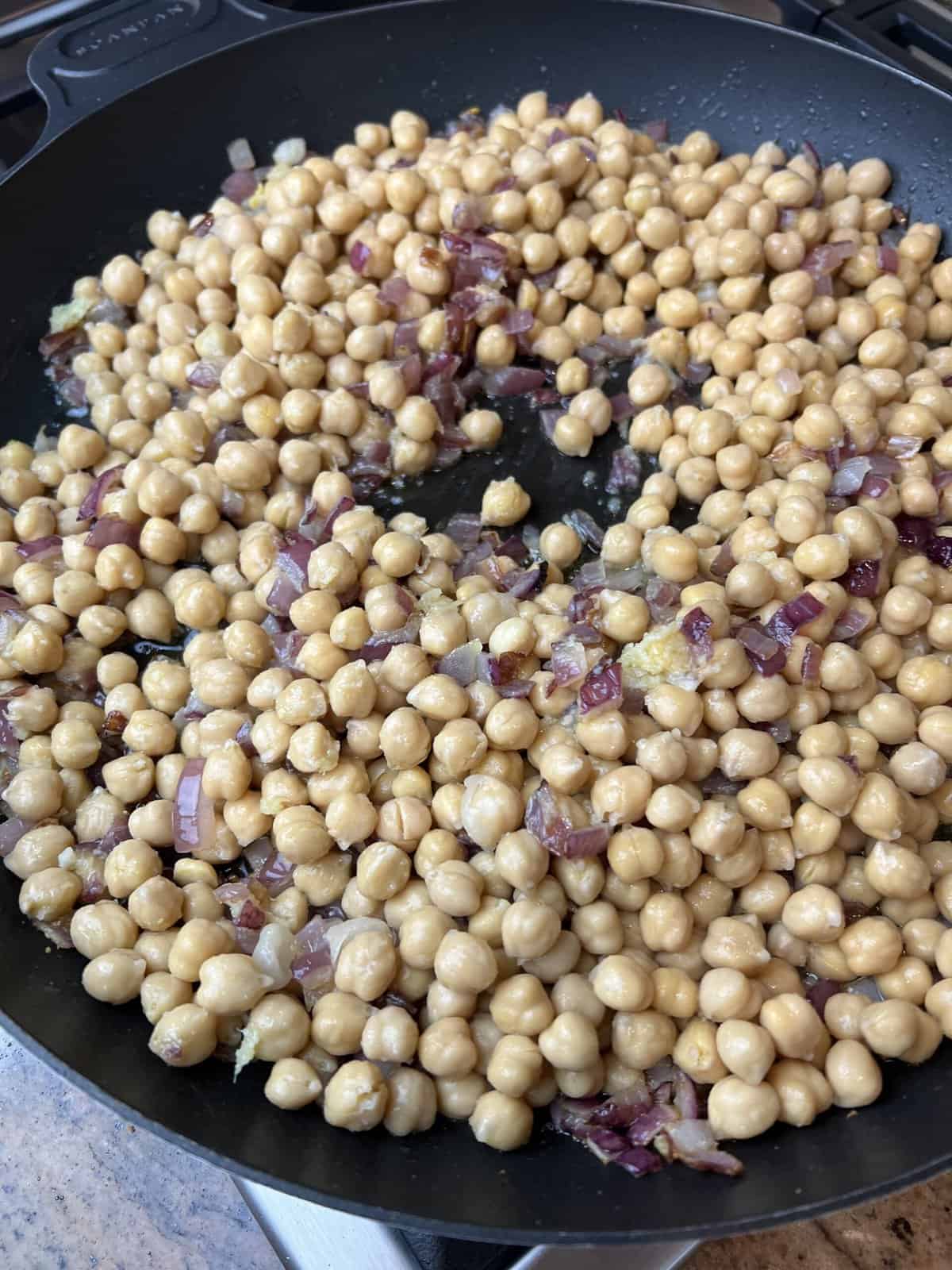 frying pan with fried onion base and boiled chickpeas.