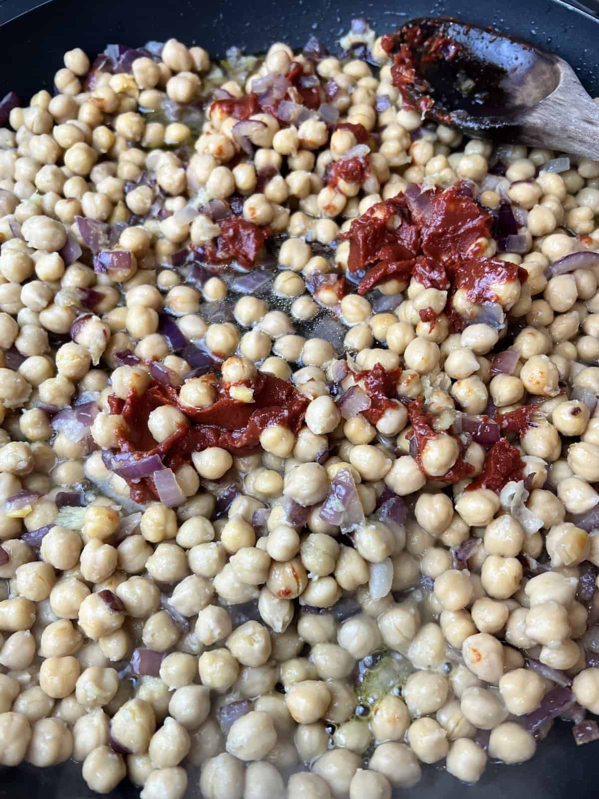 frying pan with cooked onion paste, boiled chickpeas and red tomato paste.