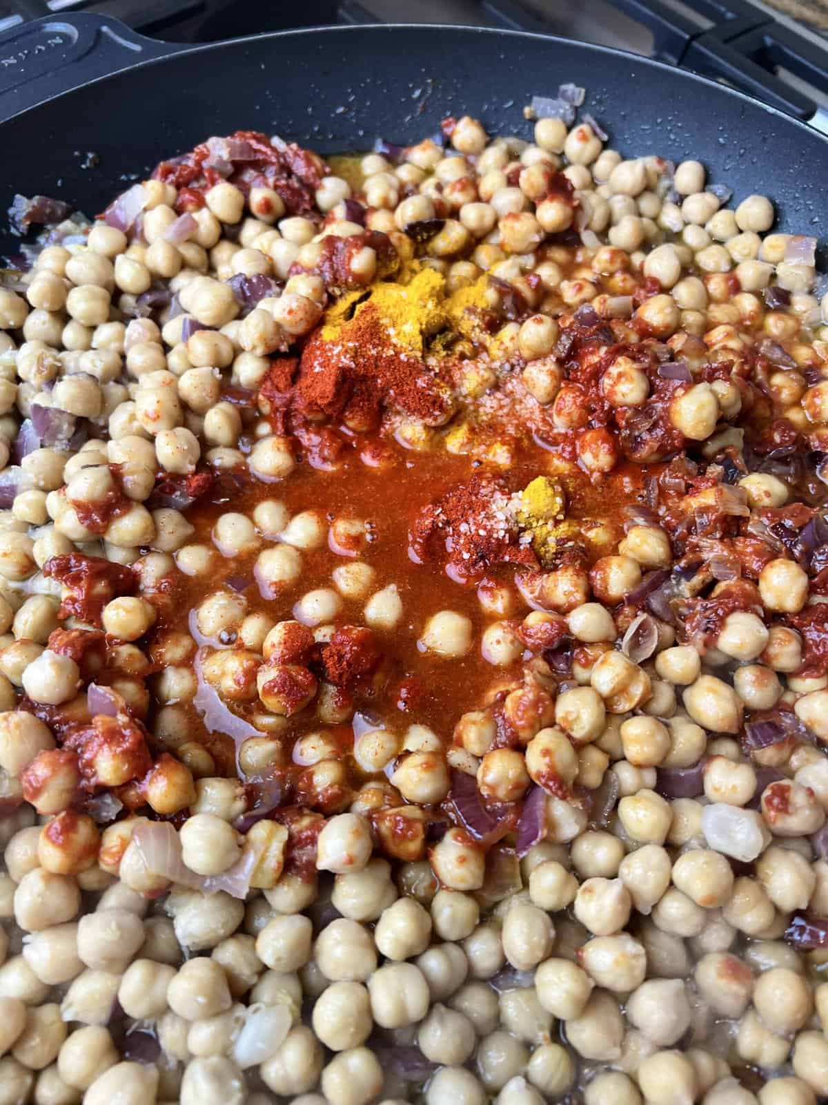 black pan with cooked onion paste, boiled chickpeas, tomato paste and spice powders.