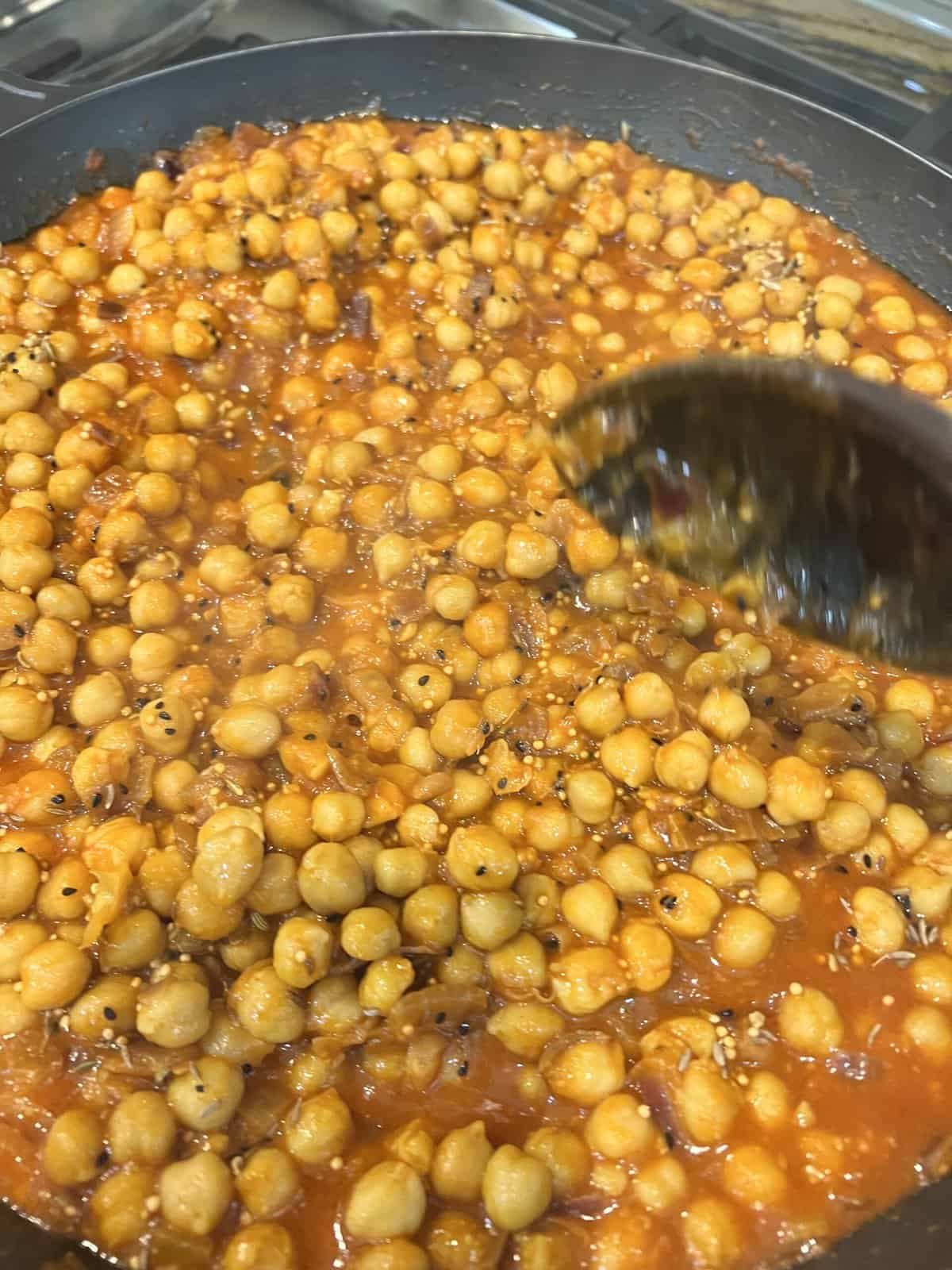 black pan with chana masala and wooden spoon.