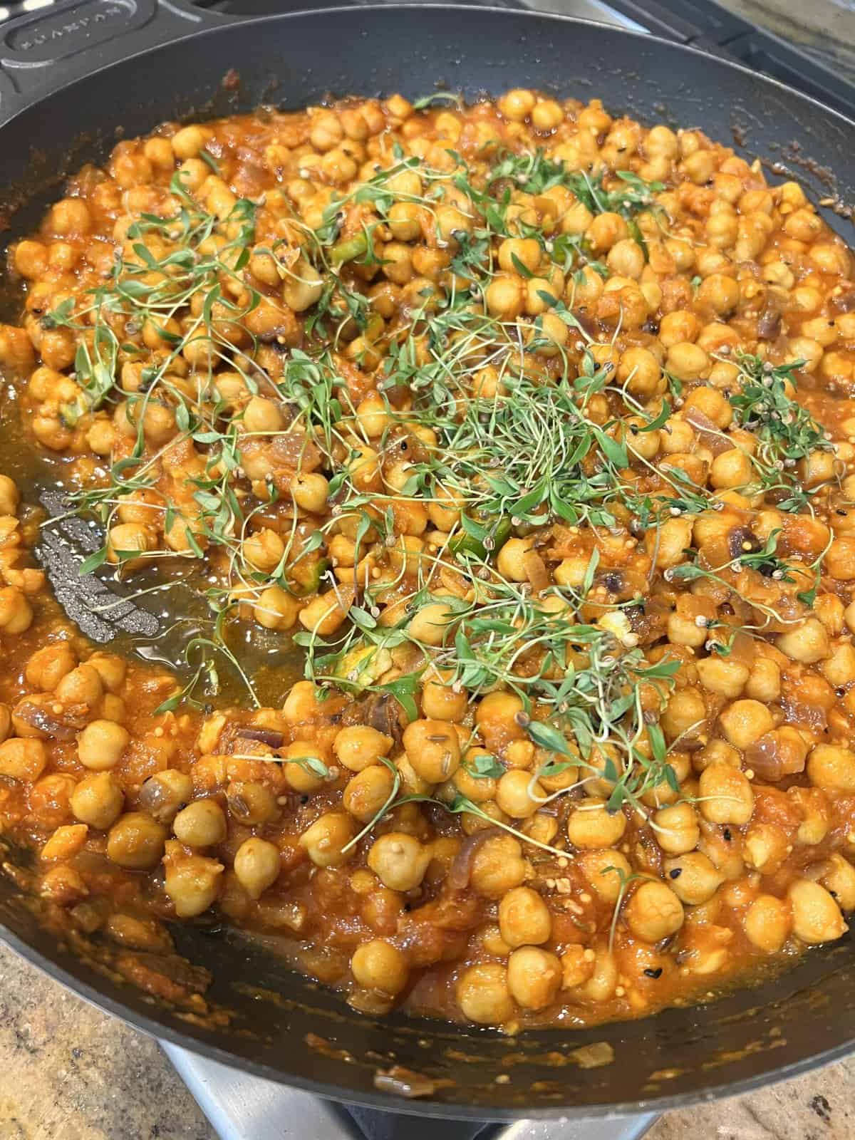 cooked chana masala in a black pan with a cilantro garnish.