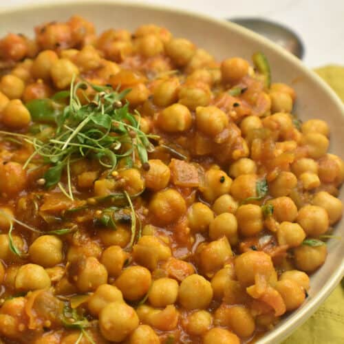 white bowl with a chickpea curry topped with cilantro microgreens.