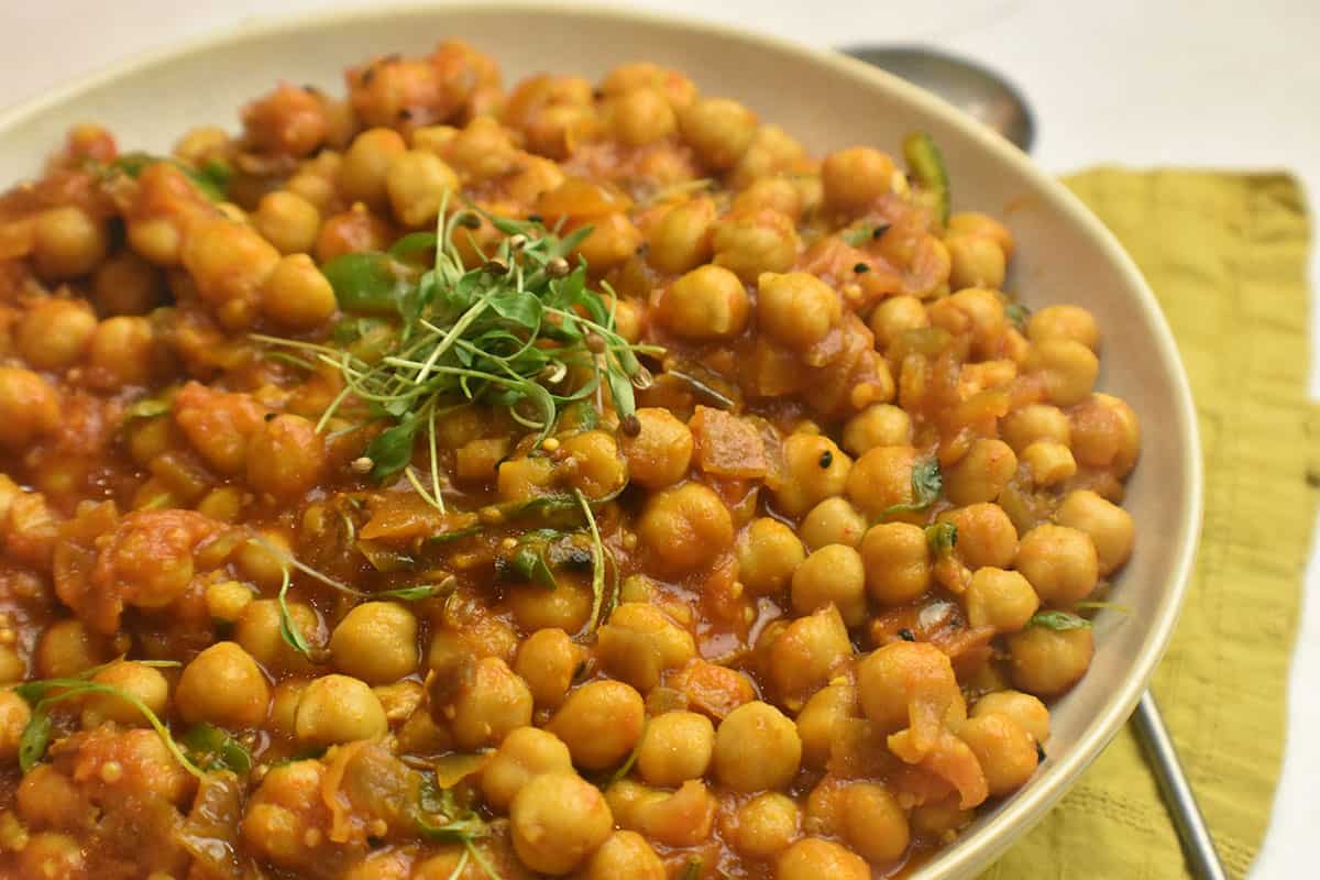 white bowl on a yellow napkin with a chickpea curry topped with cilantro microgreens.