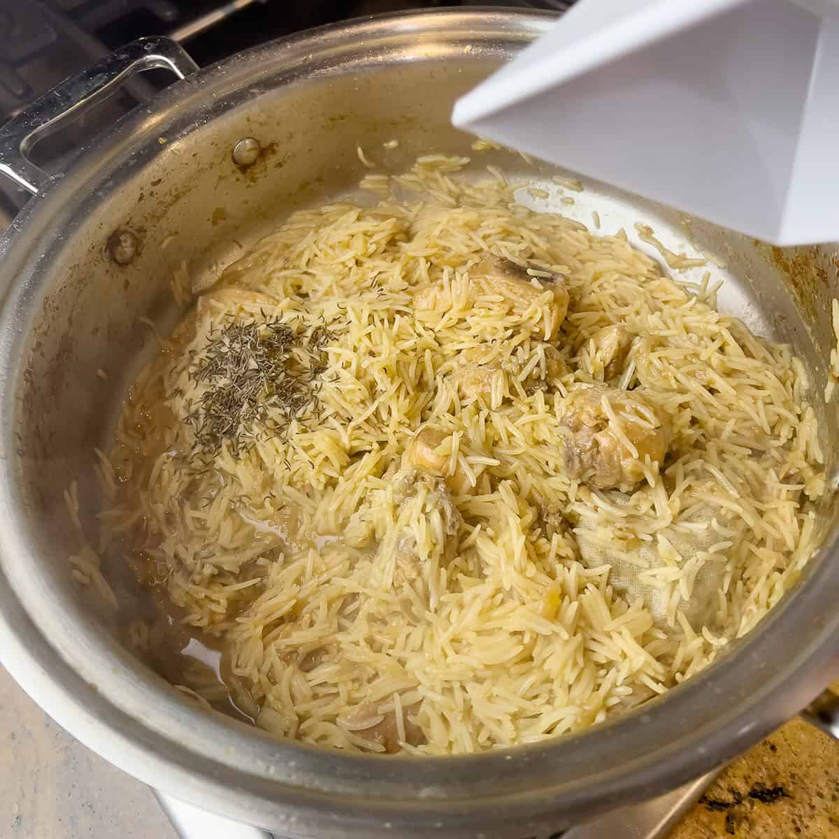 Black cumin seeds are being added to a pot of chicken and rice.