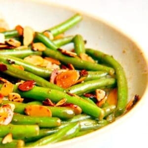 A neutral-colored bowl filled with sauteed green beans topped with toasted almonds for a green bean almondine recipe.