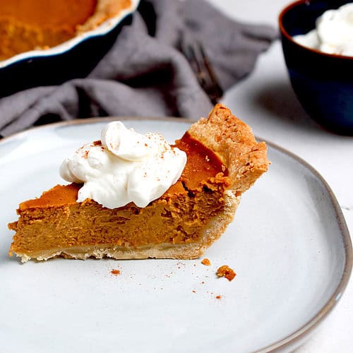 A freshly baked slice of homemade pumpkin pie is plated and ready to be served.