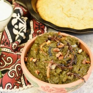sarson ka saag (mustard greens) are being served in a small clay bowl with some savory cornbread and yogurt.