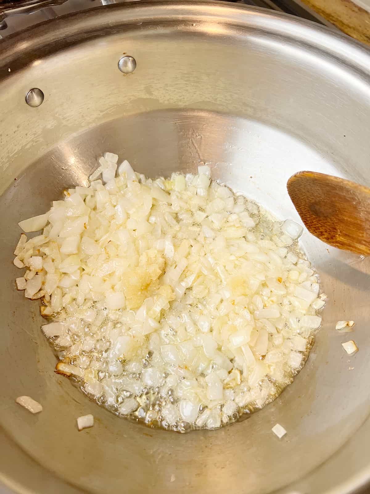 yellow onions and garlic paste being sauteed in a stainless steel cooking pot to create a base for sweet potato and black bean chili.