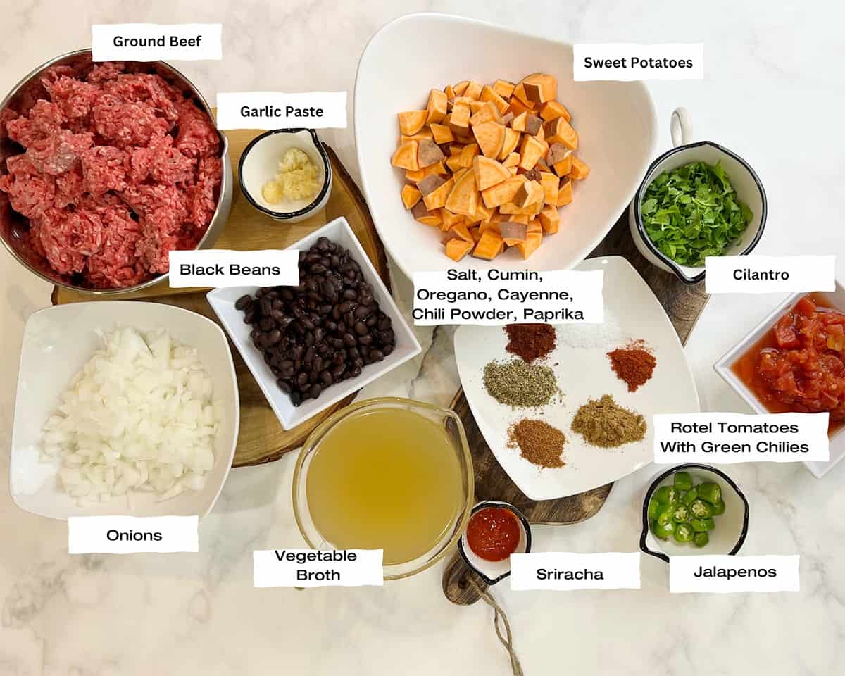 white countertop with bowls filled with ground beef, chopped onions, garlic paste, black beans, diced sweet potatoes, spices, broth, rotel tomatoes, sriracha, chopped jalapenos and cilantro to cook sweet potato and black bean chili.
