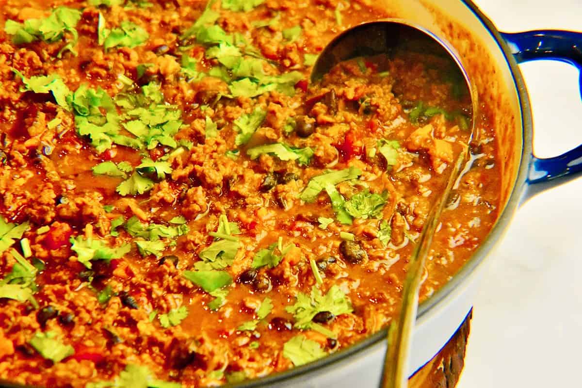 sweet potato and black bean chili garnished with cilantro in a blue cooking pot with a silver ladle in it.