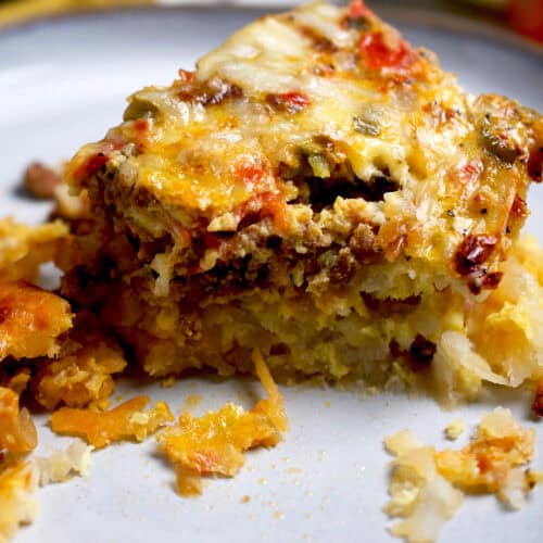 A piece of a breakfast casserole prepared with eggs, hash browns, cheese, ground beef and vegetables.