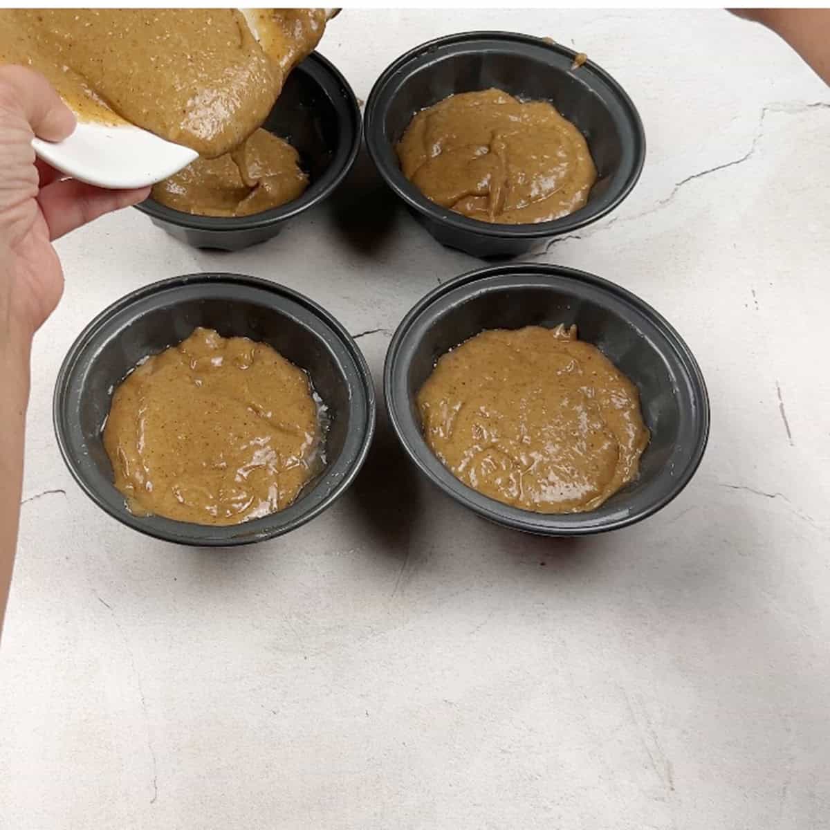 A spiced holiday cake batter is being poured into mini bundt pans.