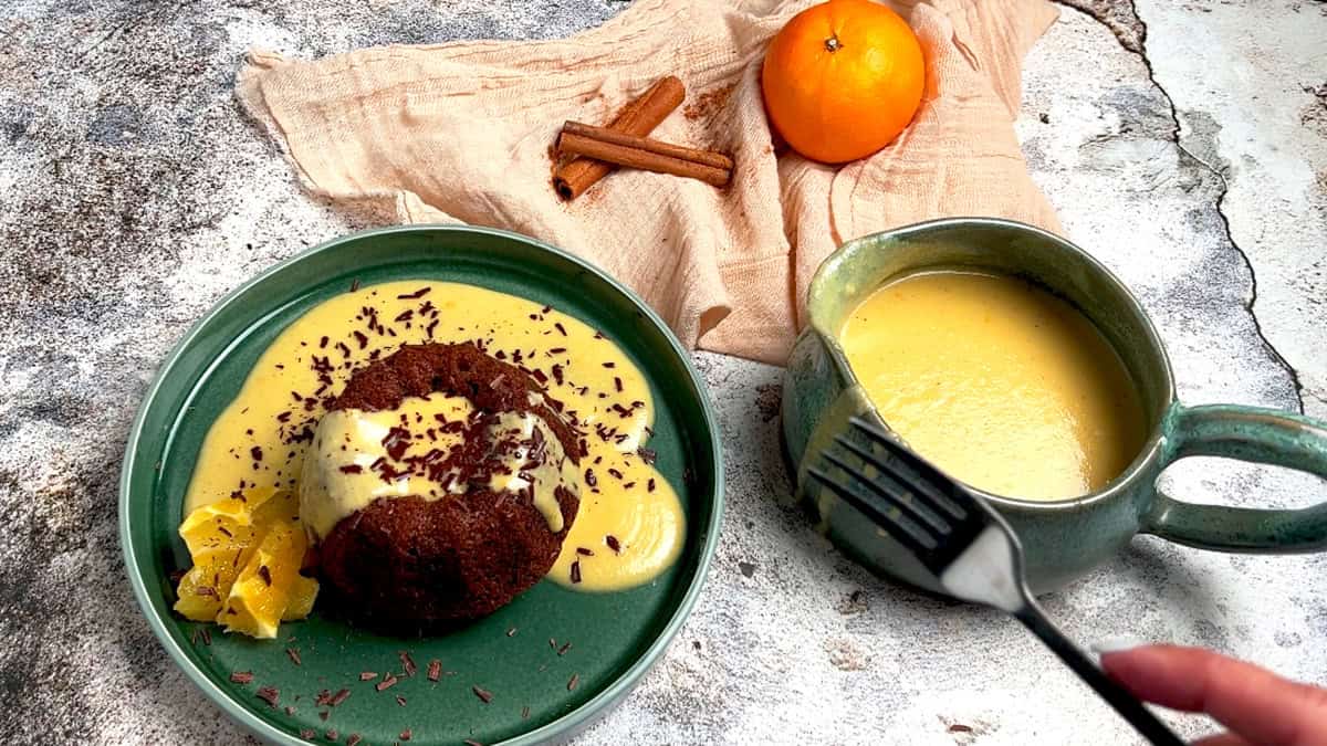 A spiced mini bundt cake is served with orange creme anglaise, oranges and chocolate flakes.