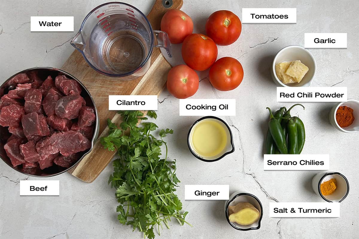 Ingredients to cook a beef recipe are resting on a white marble kitchen counter.