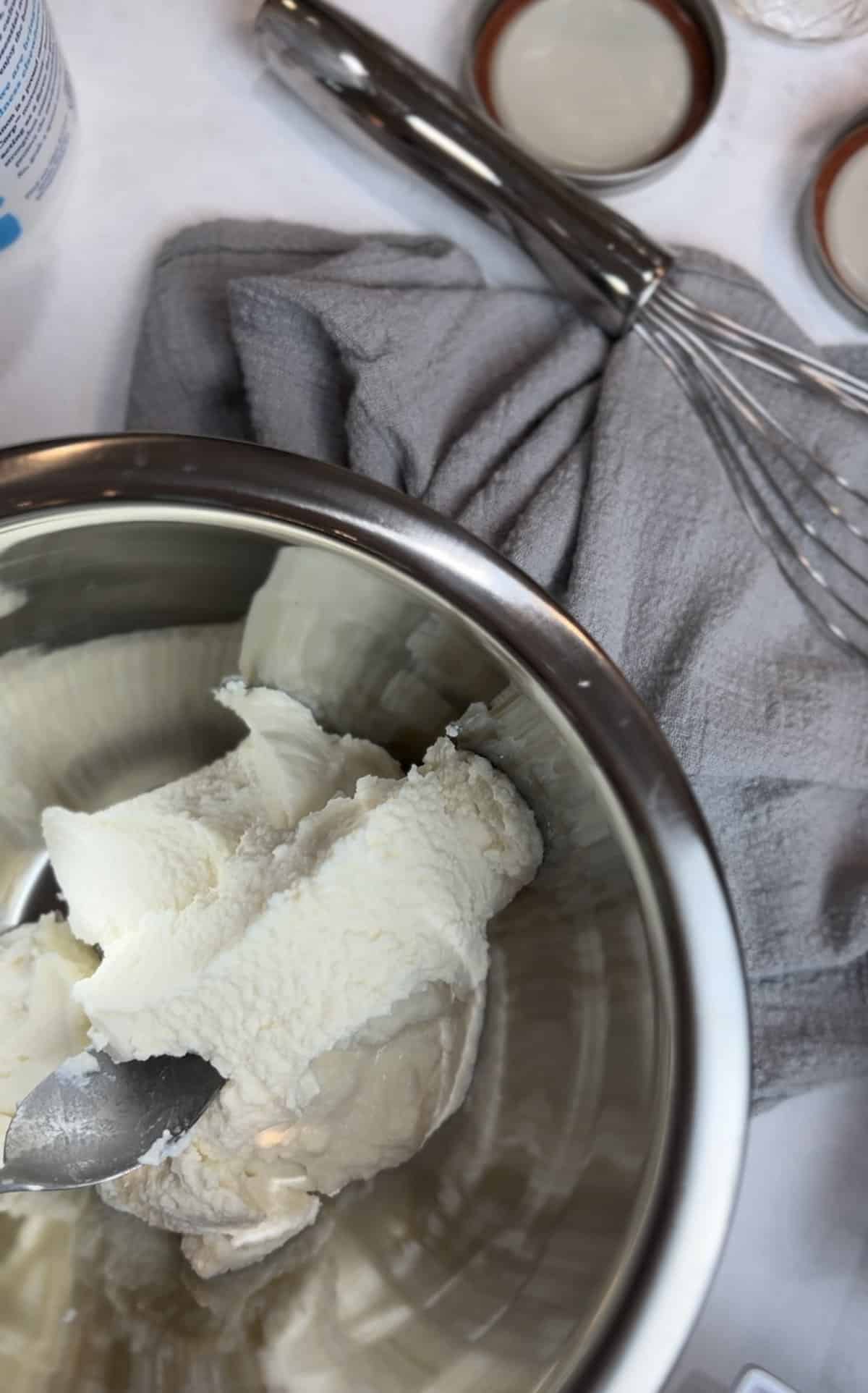 silver bowl filled with ricotta on a white counter with a grey napkin.