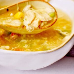 A white countertop with a white bowl filled with cooked chicken corn soup being spooned to eat.