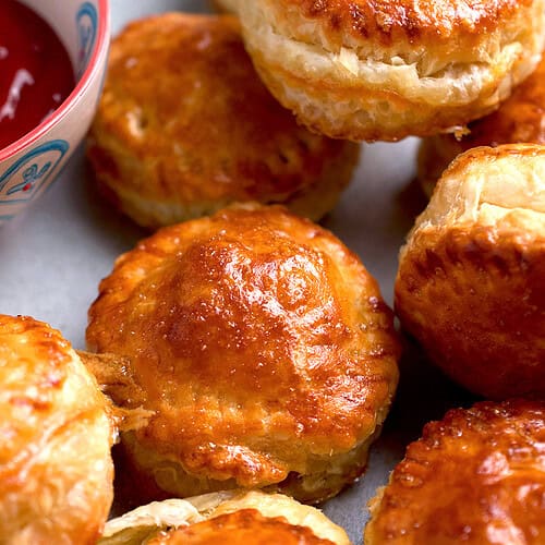 Chicken puff pastries are plated on a white platter and served with ketchup.