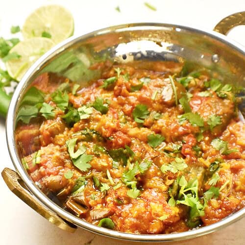 A Pakistani eggplant curry is served in a copper bowl with a garnish of cilantro and a drizzle of lime juice.