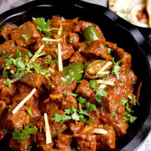 Freshly cooked karahi gosht in a black skillet resting on a greay napkin with naan next to it.