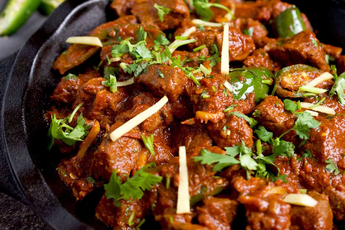 Freshly cooked beef karahi gosht is plated in a black skillet with a garnish of julienned ginger and cilantro.