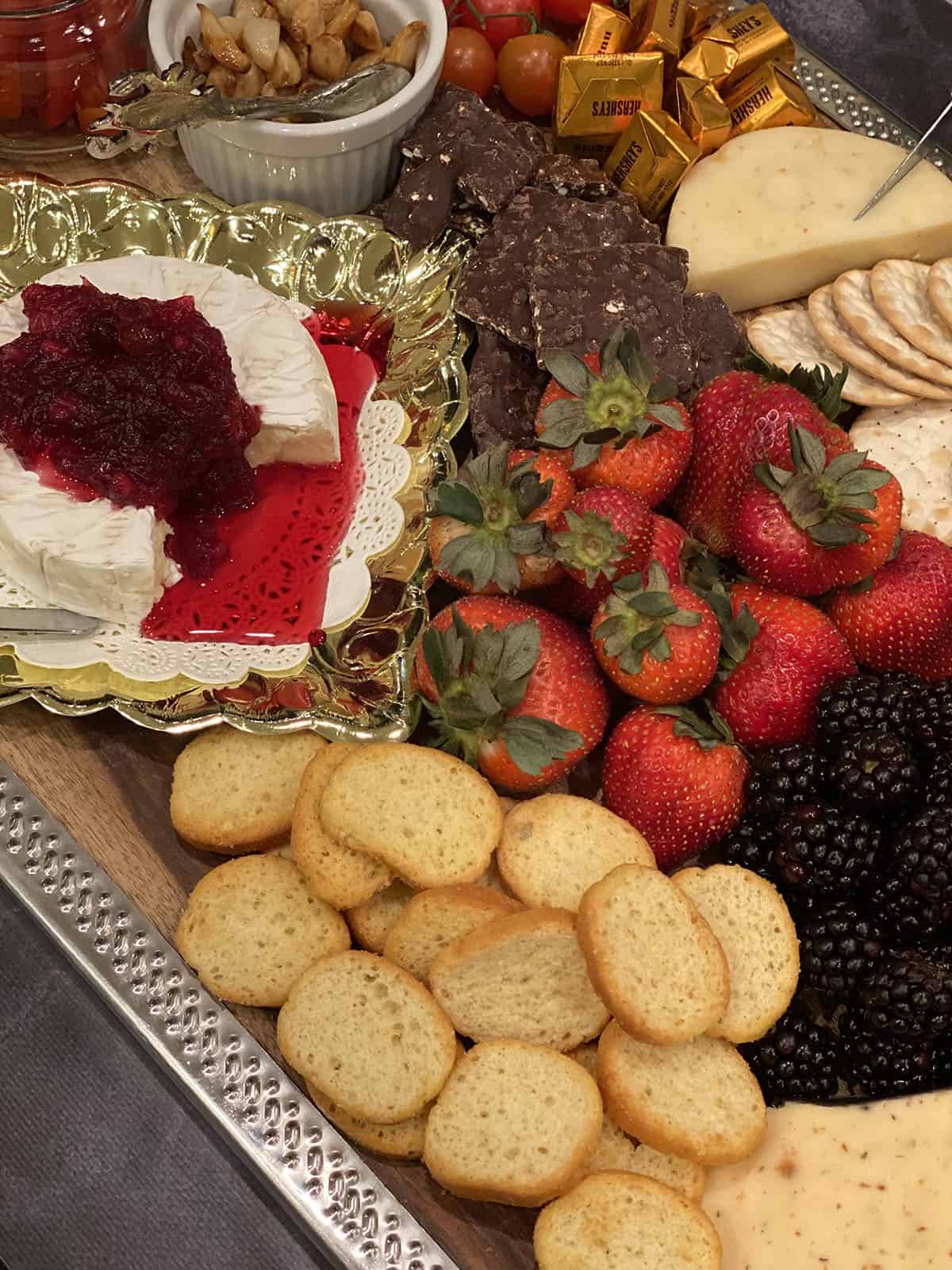 wood and silver board with strawberries, blackberries, assorted cheeses, roasted garlic, cranberry sauce, chocolate and crackers