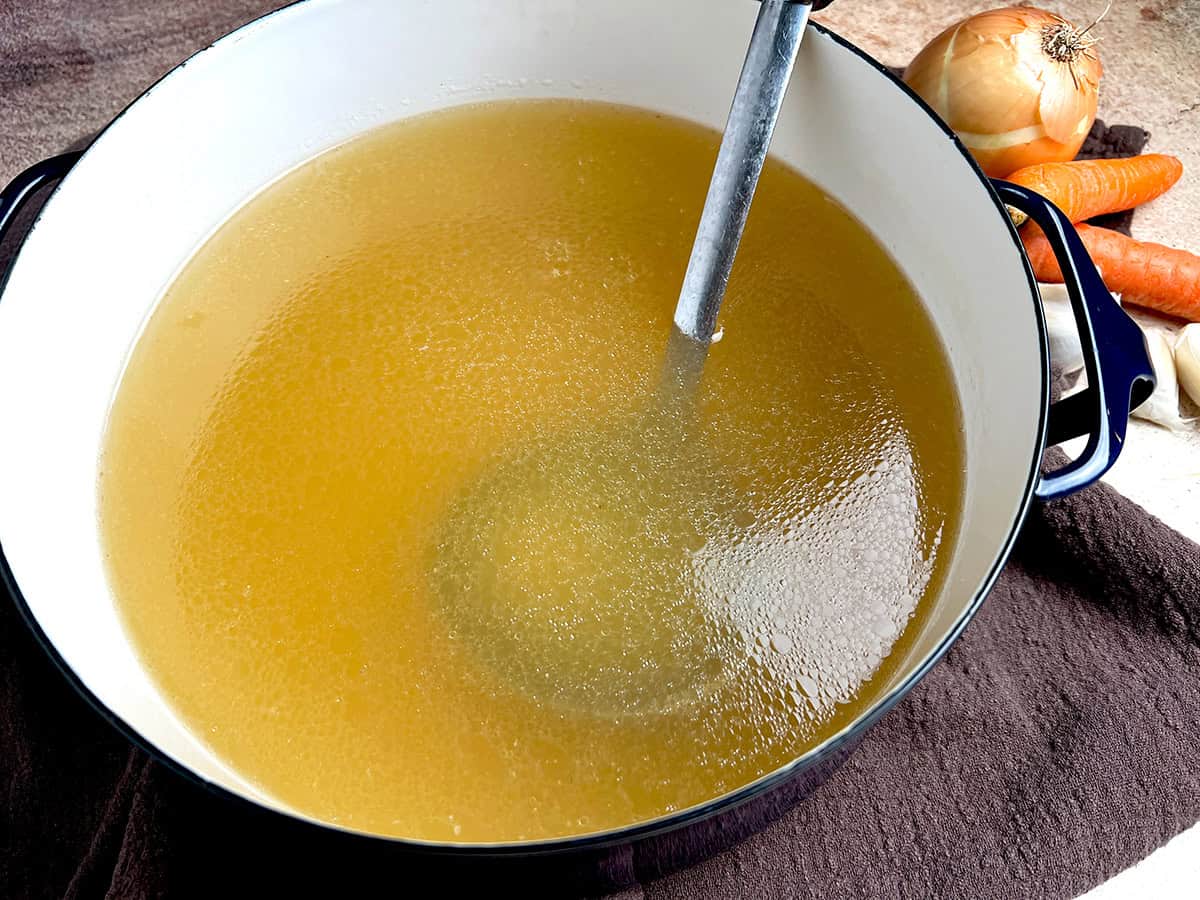 Homemade chicken broth in a large blue pot.