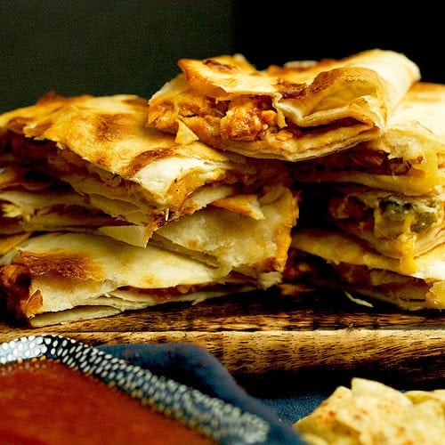 Sliced chicken and cheese quesadillas are being served with a dipping sauce on the side.