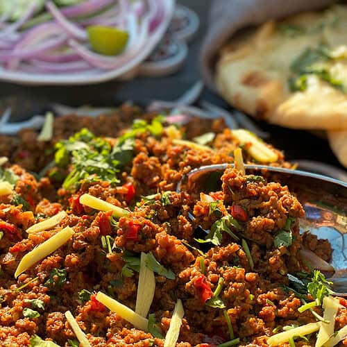 A ground beef recipe cooked as a stir fry is served with naan, onions, and limes.