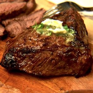 An air fryer sirloin steak topped with compound butter is resting on a chopping board with half of it cut into slices.