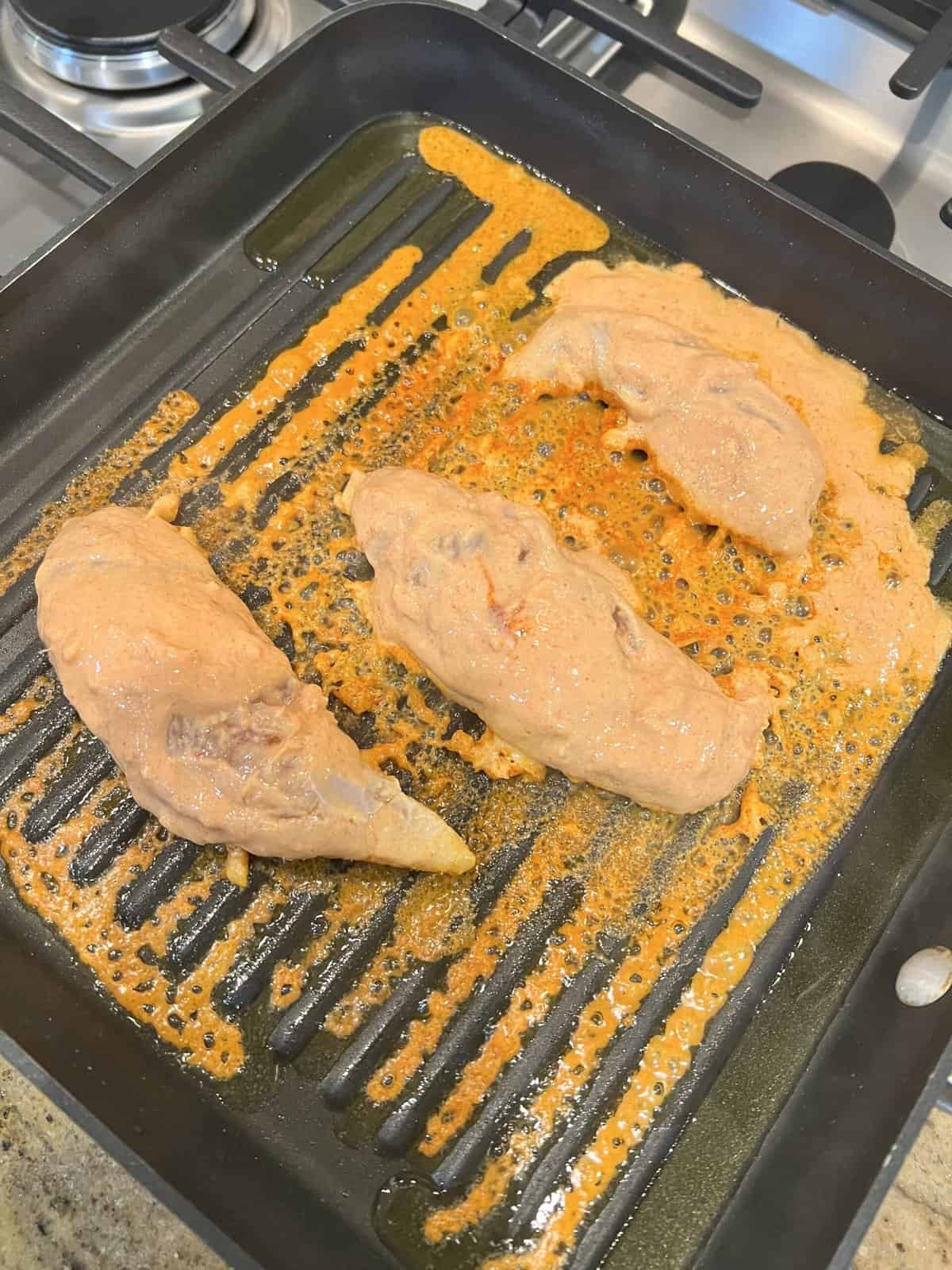black grill pan with marinated chicken tenderloins caoted in orange marinade.