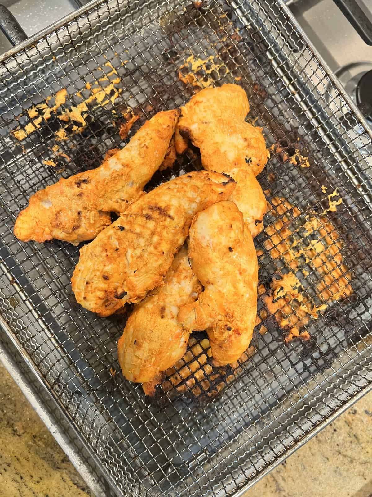 cooked chicken tikka tenderloins in air fryer tray.