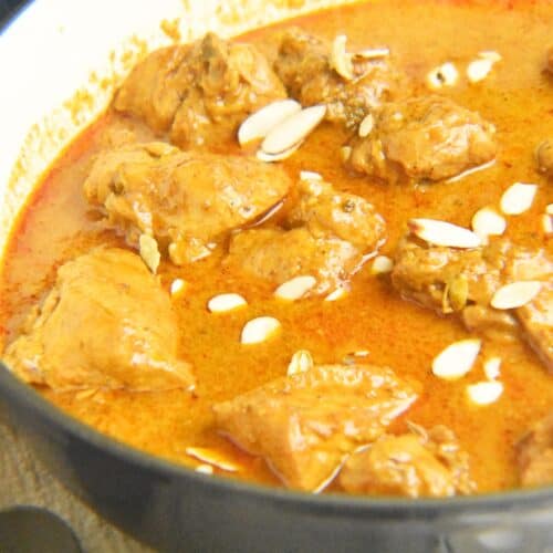 Chicken Korma garnished with almonds in a blue pot resting on a grey napkin with a roti on the side.