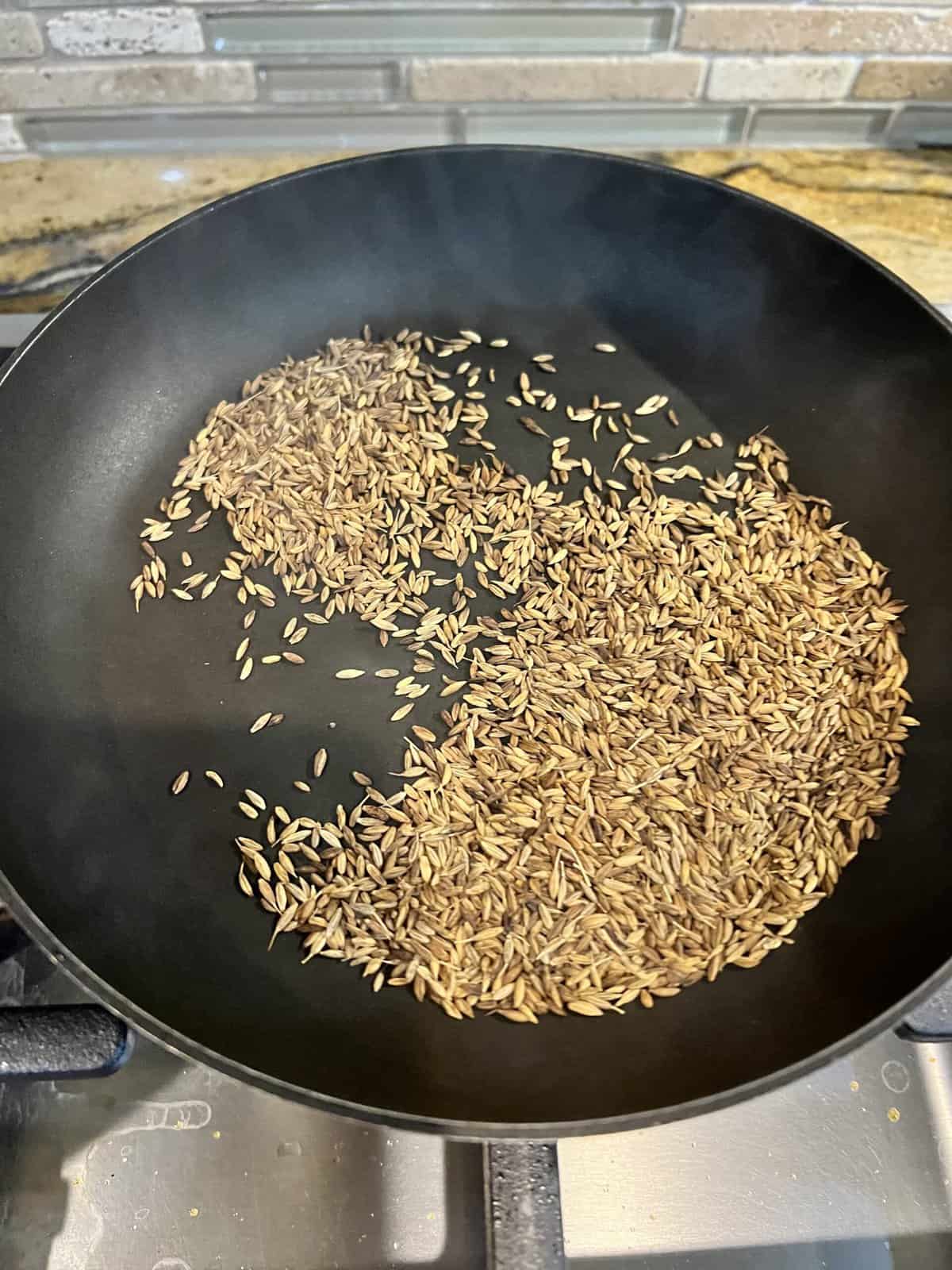 roasting cumin seeds in a black pan.