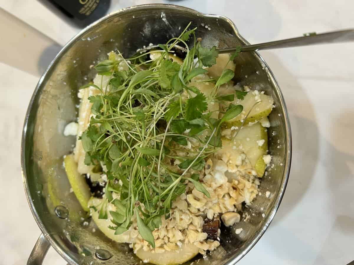microgreens on top of a pear salad in a metal bowl.