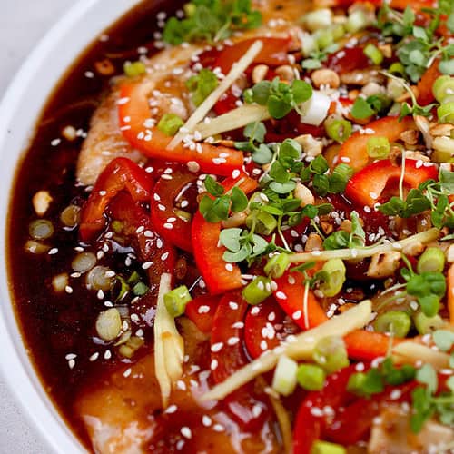 A plated Thai fish recipe with tamarind sauce garnished with red bell pepper, green onions, basil and chopped peanuts.