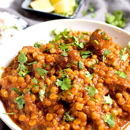 A dal gosht recipe is plated in a white bowl and garnished with cilantro, ready to be eaten.