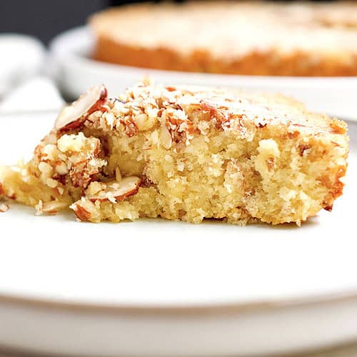 A slice of a freshly baked almond cake is plated in a white plate.