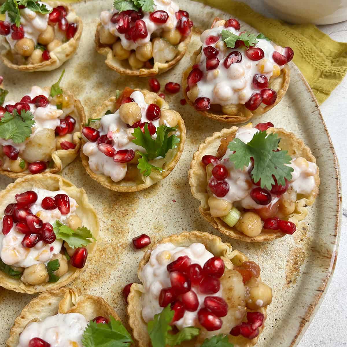 Baked papdi chaat appetizer cups are plated and garnished with pomegranates and cilantro.