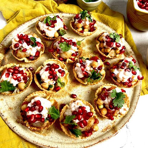 Freshly made appetizer cups filled with chana chaat, boondi raita and garnished with pomegranate seeds and cilantro are plated and ready to be served.