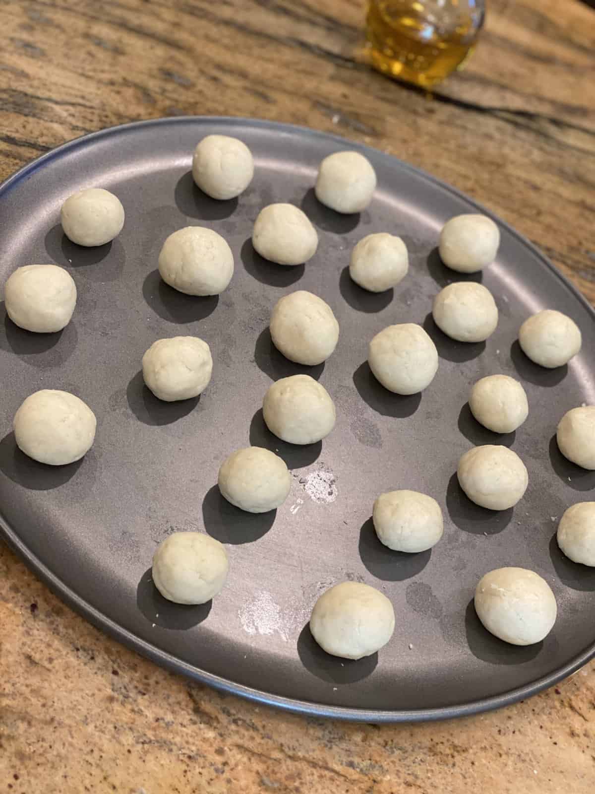 Brown granite counter with a metal tray filled with dough shaped into tiny gulab jamun.