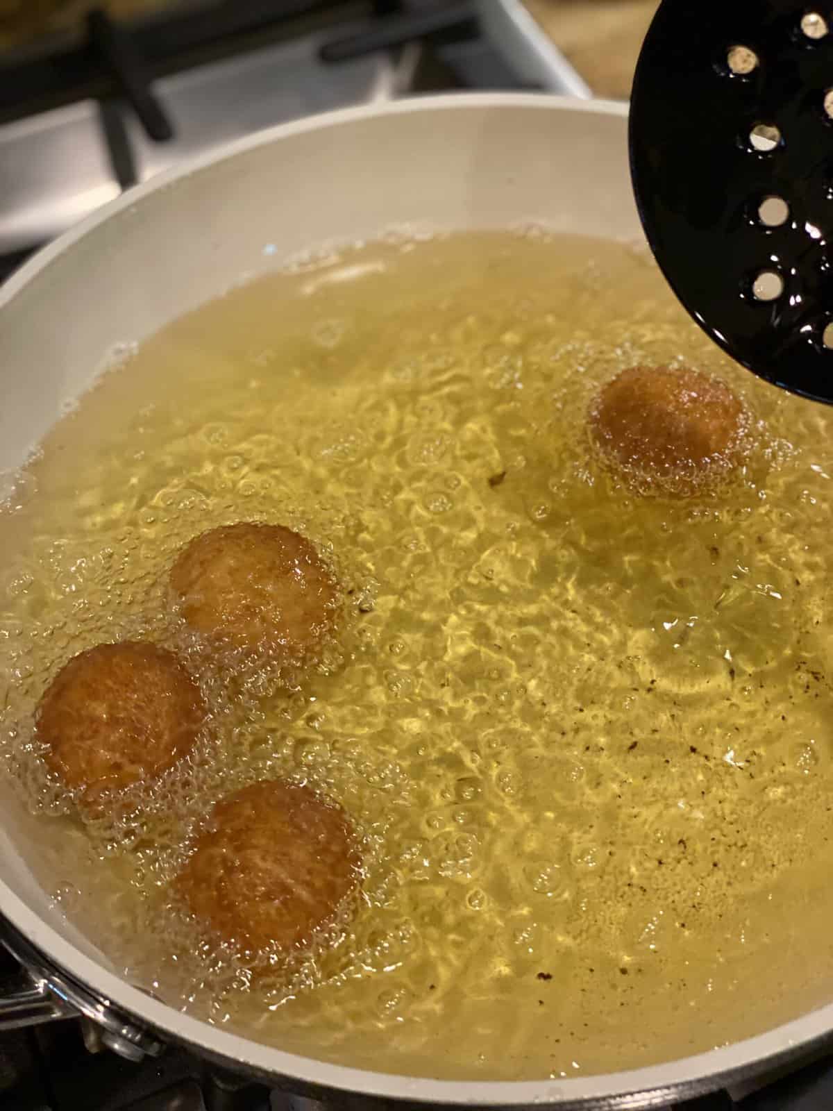 A deep cooking pot filled with hot oil and nicely browned gulab jamun.